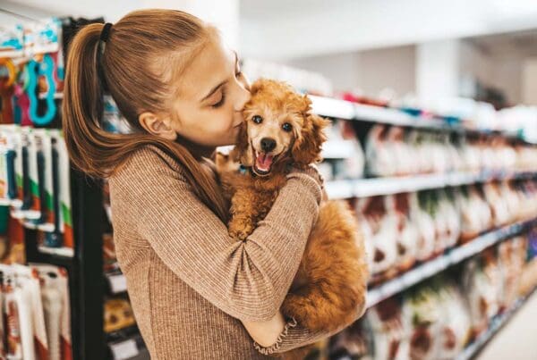 Pet Business Insurance - Young and Joyful Girl Shopping in a Pet Store with Her New Poodle Puppy and Giving Him with a Kiss